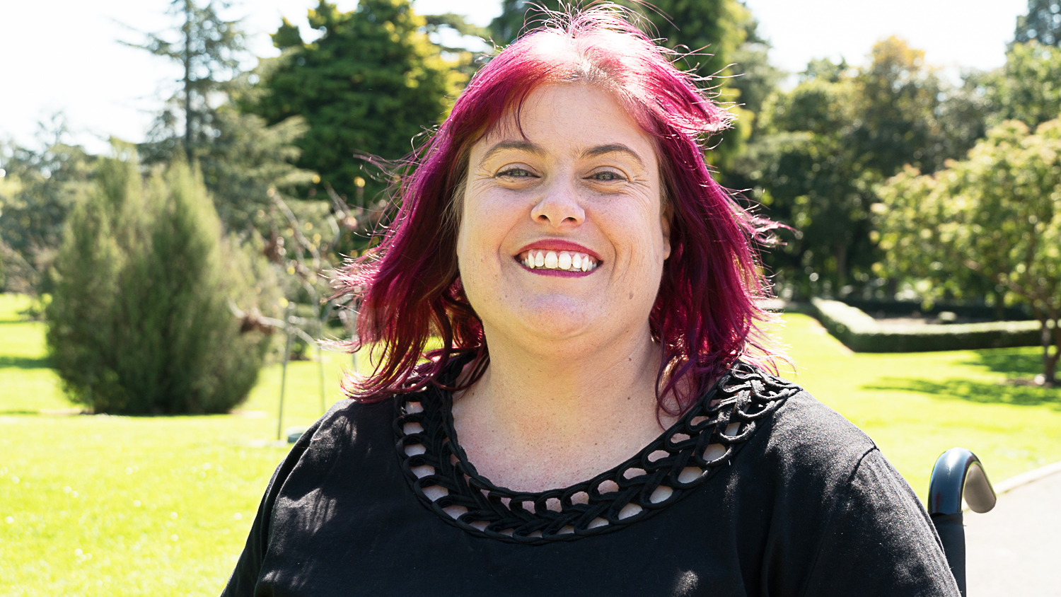 Photo of Christine Priest outside with a huge smile and purple hair