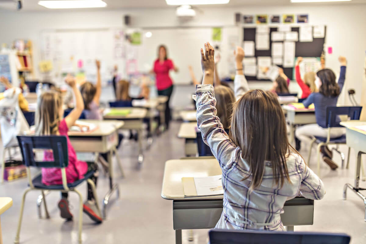 Children raising their hands in a classroom.