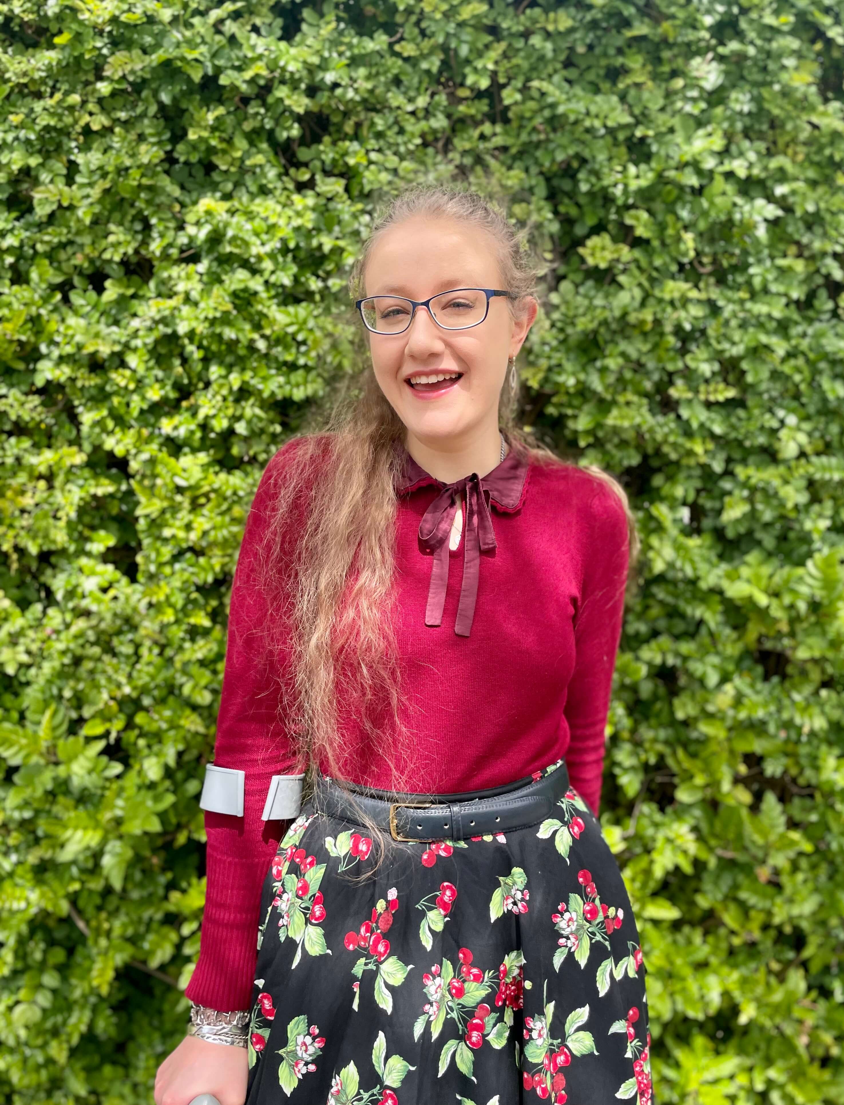 Photo of Ally in front of green wall, smiling at camera.