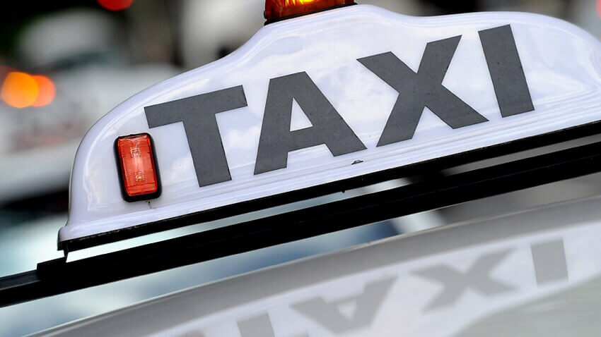 Photo of a white sign with words Taxi atop of a taxi.
