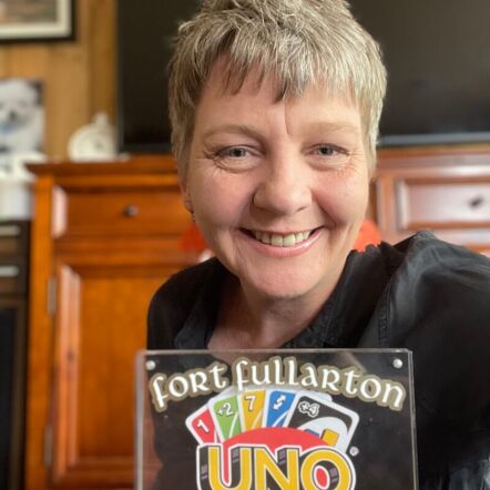 Photo of Kate, a white woman with short light blonde hair, holding a clear trophy with the Uno logo and gold text "Fort Fullarton Challenge Winner."