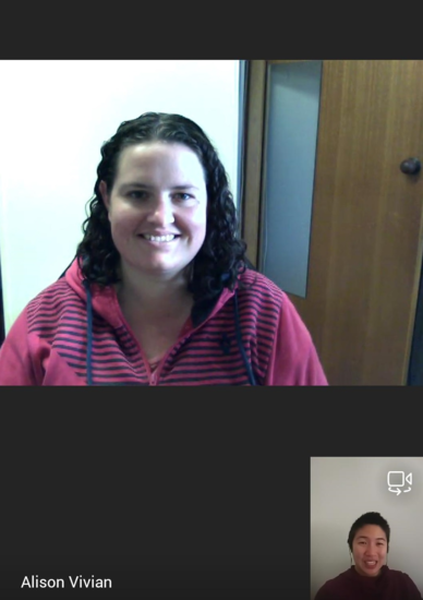 Teams call between Ali and Isabel. Ali has dark curly hair and is wearing a maroon and navy striped hoodie. Isabel is also in a maroon hoodie and has earphones in. Both are smiling at the camera.