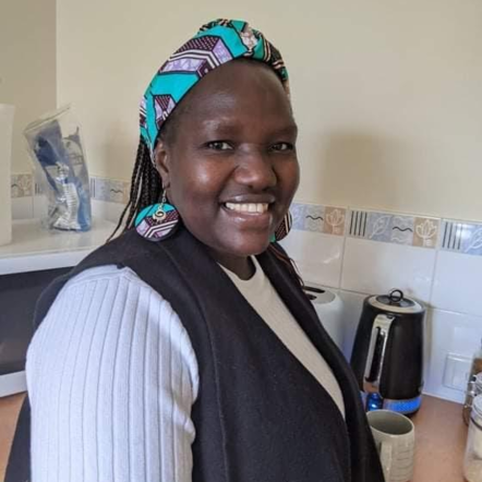 Esther, an African woman with an electric blue patterned headband and matching earrings, smiles at the camera.