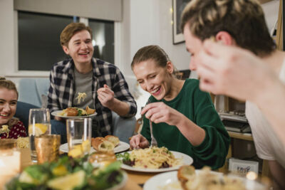 Photo shows a group of 2 men an 2 women at a table enjoying a meal together at home.