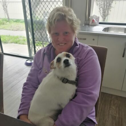 Ashley sitting in a chair at home. She is wearing a violet jumper and her dog Delta is sitting on her lap.