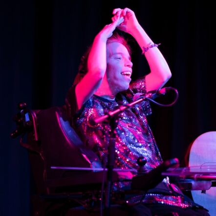 Georgia performing onstage at an event, big grin on her face and arms clasped overhead. Coloured lights catch and shimmer on her sparkly top.