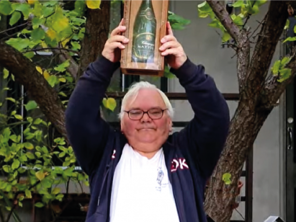 Image is Collin holding the champagne bottle trophy over his head in victory.