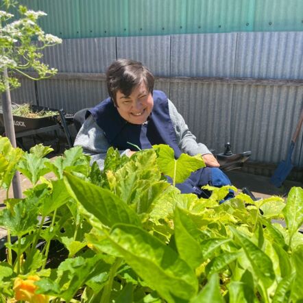 Lou smiling in her backyard garden, which is full of flowering zucchini plants.