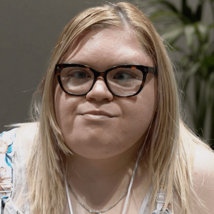 Photo of Krystal, a woman with white skin and straight long light blonde hair. She is wearing glasses,a patterned strapless top and is looking straight at the camera.