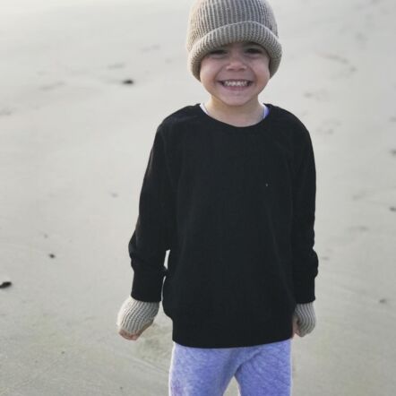 Photo shows Slade with a big smile on the beach, dressed in a black jumper and grey pants with matching olive coloured hat and gloves.