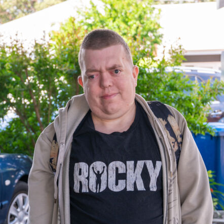 Photo shows Tim, who is wearing a black shirt with the words "Rocky" and a beige hoodie. He has brown crew cut hair.